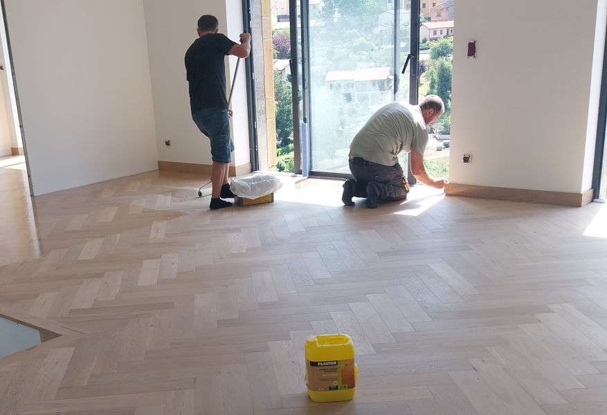 Deux professionnels sont entrain de vitrifier un parquet contrecollé chêne bâtons rompus avec un verni Plastor effet bois nu sur un chantier au Val d'Oingt dans le Beaujolais